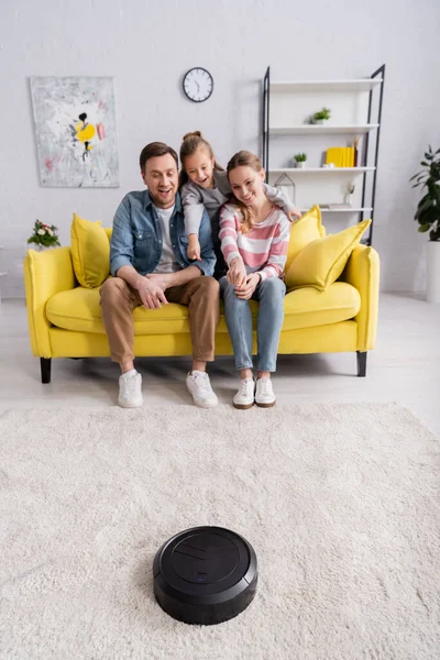 Mujer sonriente apuntando a la aspiradora robótica cerca de la familia - foto de stock