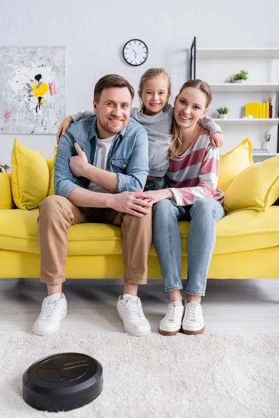 Улыбающийся ребенок обнимает родителей рядом с роботизированным пылесосом на полу — стоковое фото