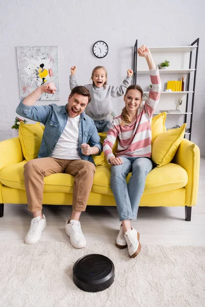 Família excitada olhando para a câmera perto de aspirador robótico em casa — Fotografia de Stock