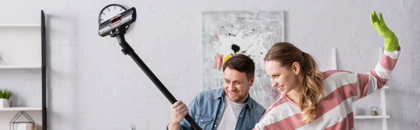 Woman in rubber glove standing near cheerful husband with vacuum cleaner, banner — Stock Photo