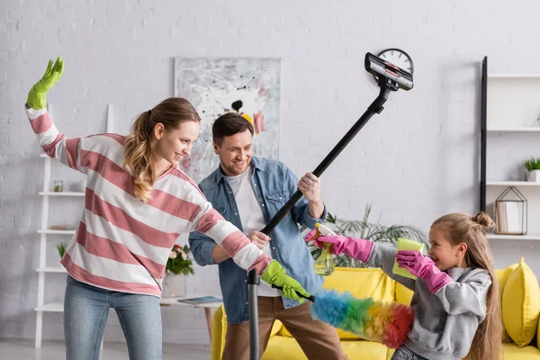 Familia positiva jugando con artículos de limpieza en casa - foto de stock