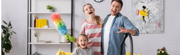 Familia asombrada con suministros de limpieza mirando a la cámara, pancarta - foto de stock