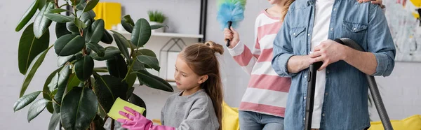 Child cleaning plant near parents with cleaning supplies, banner — Stock Photo