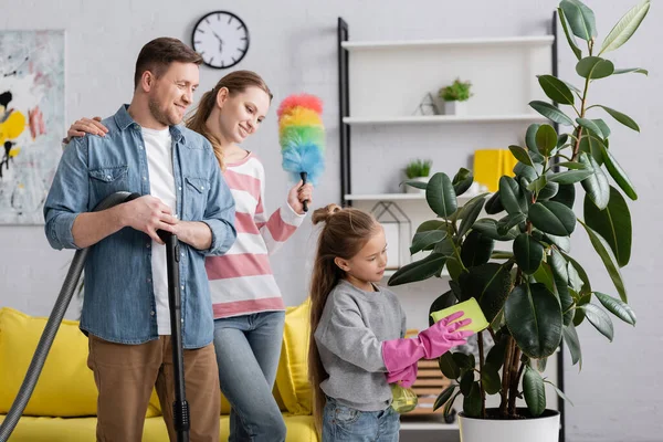 Child cleaning leaves of plant near smiling parents at home — Stock Photo