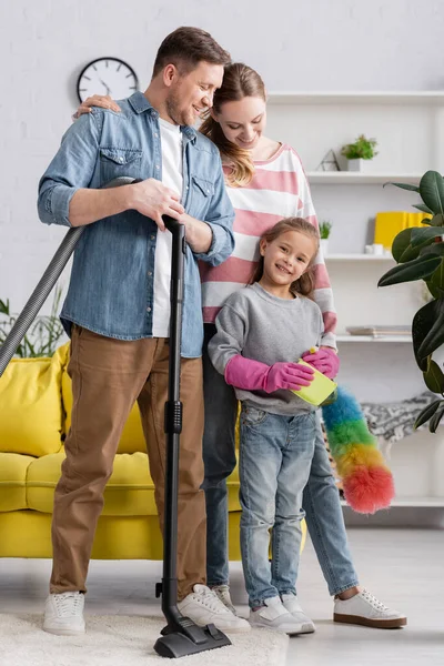 Smiling family with cleaning supplies standing in living room — Stock Photo