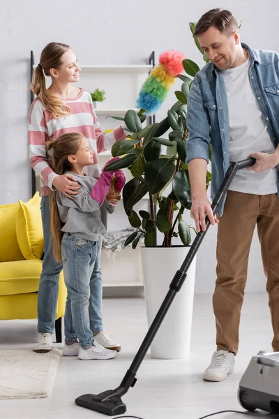 Улыбающийся мужчина чистит ковер рядом с женой и дочерью — стоковое фото