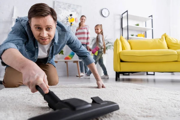 Lächelnder Mann reinigt Teppich mit Staubsauger — Stockfoto