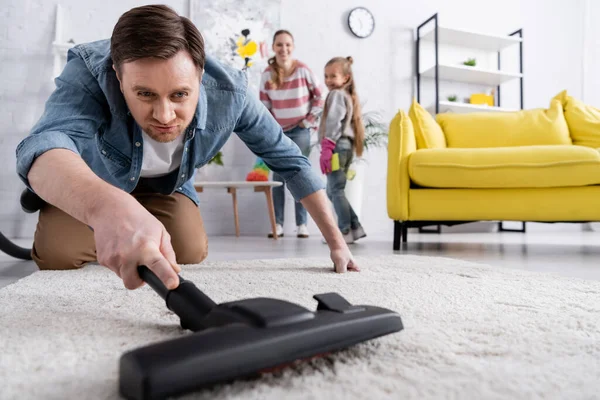 Mann putzt Teppich im verschwommenen Vordergrund bei verschwommener Familie zu Hause — Stockfoto