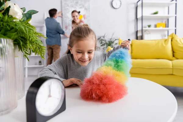 Table de nettoyage fille souriante avec brosse à poussière à la maison — Photo de stock