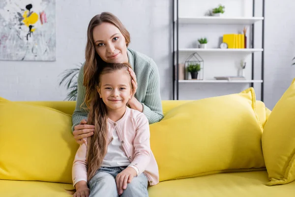 Chica feliz mirando a la cámara cerca de los padres en el sofá amarillo - foto de stock