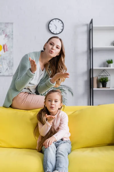 Mother and kid blowing air kiss at camera on couch — Stock Photo