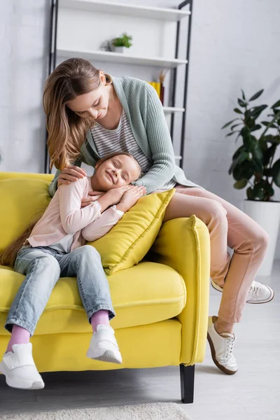 Mulher abraçando filha com olhos fechados no travesseiro no sofá — Fotografia de Stock