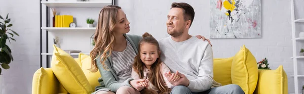 Famille souriante assise sur un canapé jaune à la maison, bannière — Photo de stock