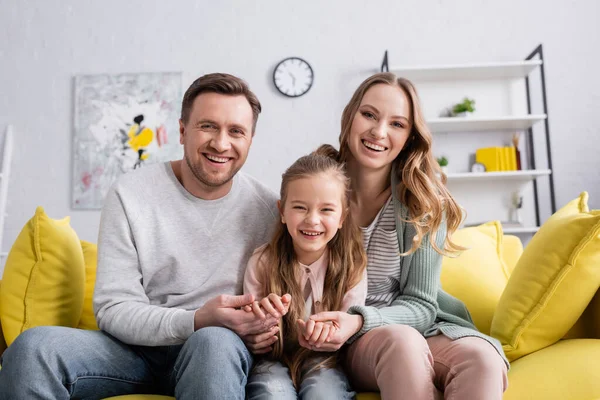 Familia con hija sonriendo a la cámara en la sala de estar - foto de stock