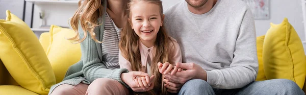 Sonriente niño cogido de la mano de los padres en el sofá, pancarta - foto de stock