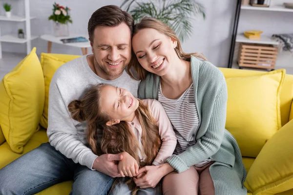 Famiglia felice con gli occhi chiusi che si abbracciano sul divano — Foto stock