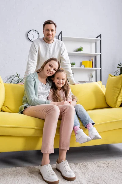 Femme étreignant enfant sur le canapé jaune près mari souriant — Photo de stock
