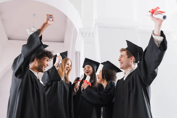 Cheerful multiethnic graduates with diplomas in university — Stock Photo