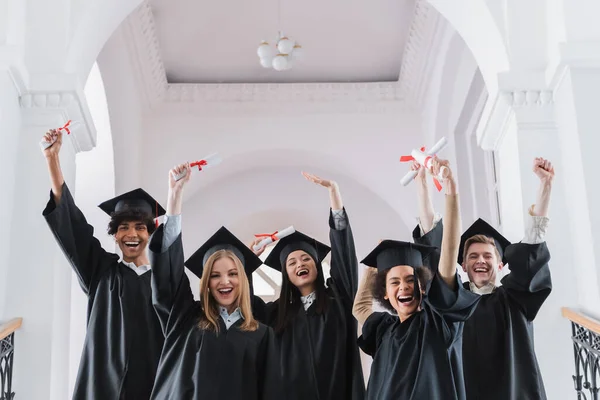 Emocionados estudiantes multiculturales con diplomas que muestran sí gesto - foto de stock