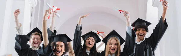 Estudiantes multiétnicos con diplomas que muestran sí gesto, pancarta - foto de stock