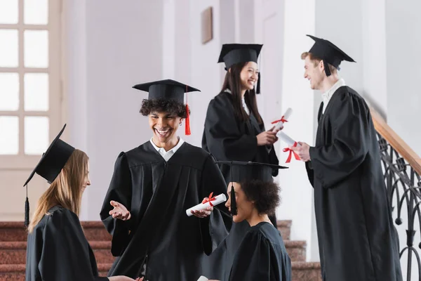 Positif afro-américain diplômé en chapeau parler à des amis à l'université — Photo de stock