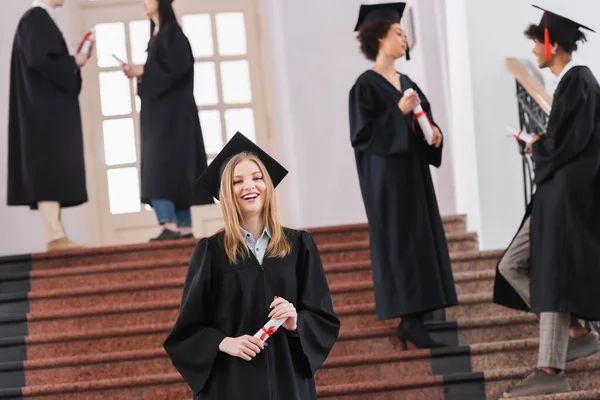 Estudiante feliz sosteniendo diploma durante la graduación en la universidad - foto de stock