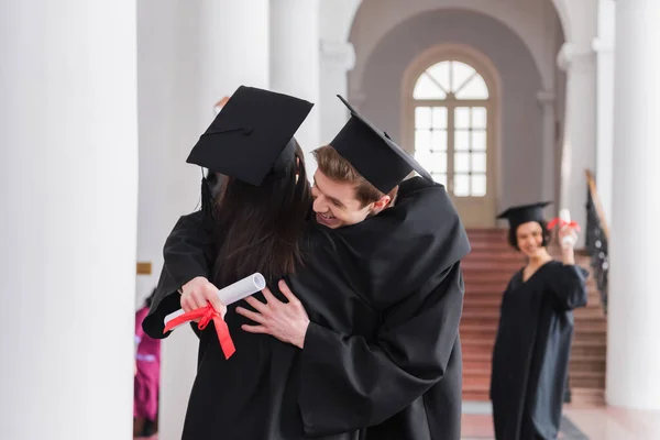 Graduado sonriente con un amigo abrazador de diploma - foto de stock