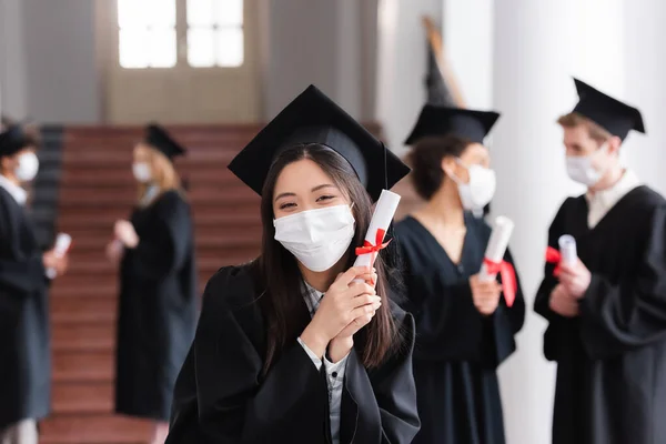 Asian bachelor in protective mask holding diploma in university — Stock Photo