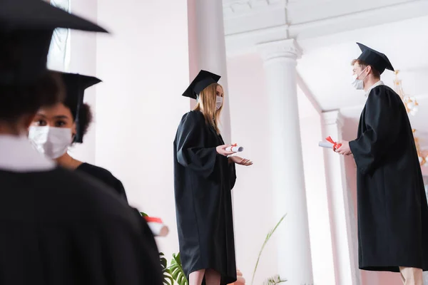 Bachelors in medical masks talking near multiethnic friends on blurred foreground — Stock Photo