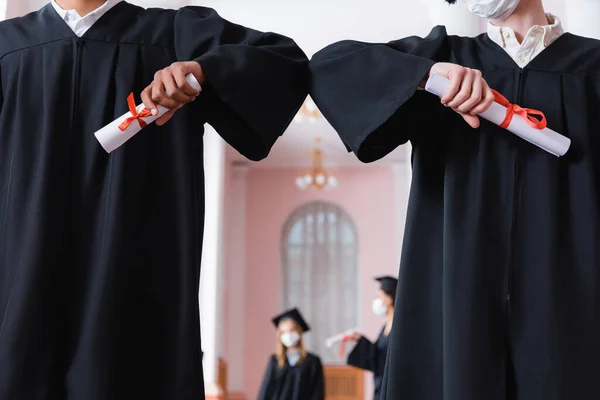 Cropped view of multiethnic graduates with diplomas doing embow bump — Stock Photo