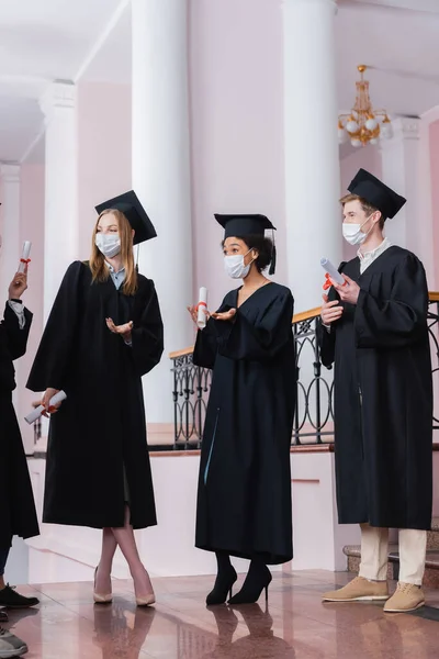 Межрасовые холостяки в медицинских масках выступают в зале университета — стоковое фото