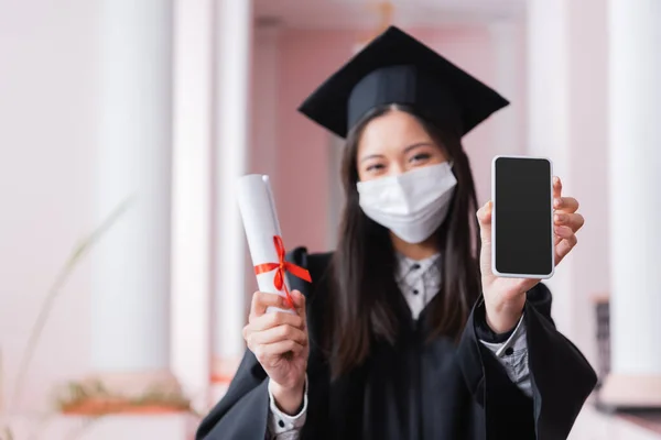 Smartphone et diplôme dans les mains de diplômés asiatiques sur fond flou — Photo de stock