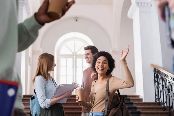 Estudiante afroamericano con café saludando mano a amigo en la universidad - foto de stock