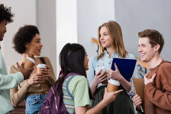 Positive multicultural students with paper cups talking in hall — Stock Photo