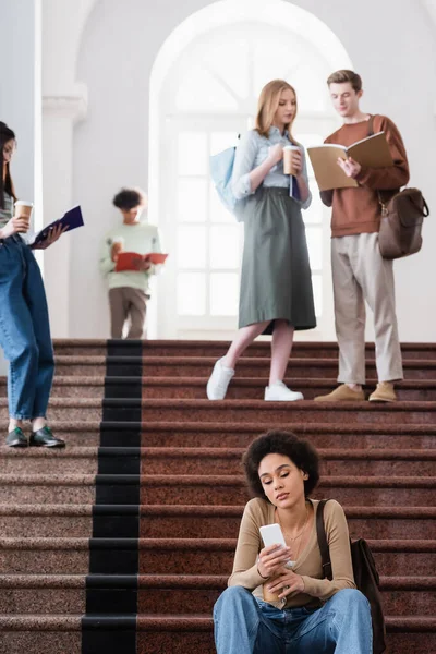 African american student using smartphone on stairs in university — Stock Photo