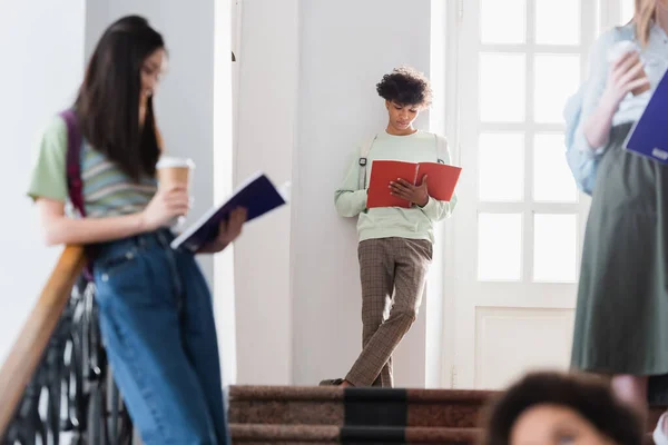 African american student holding notebook near blurred people on blurred foreground — Stock Photo