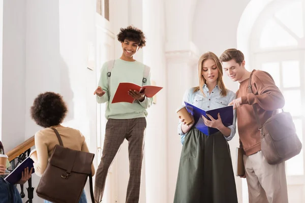 African american student with notebook smiling near friends in university — Stock Photo