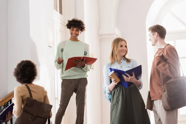 Afroamerikanische Studentin mit Notizbuch steht in der Nähe von Freunden und spricht in der Universität — Stockfoto