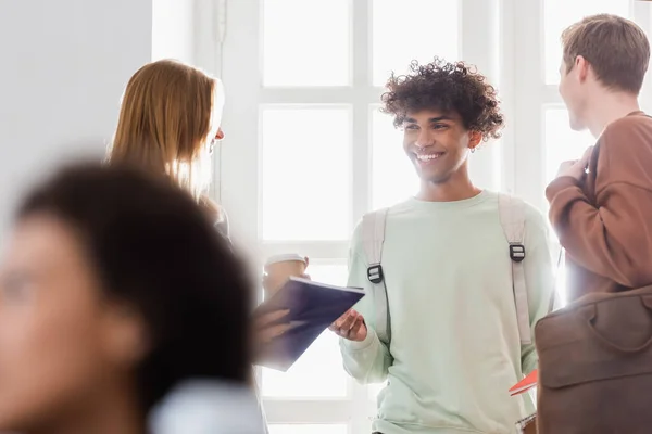 Smiling african american student standing near friends and window in university — Stock Photo