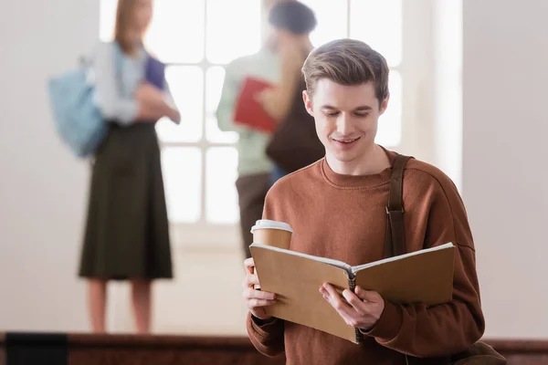 Lächelnder Student mit Pappbecher und Notizbuch in der Universität — Stockfoto