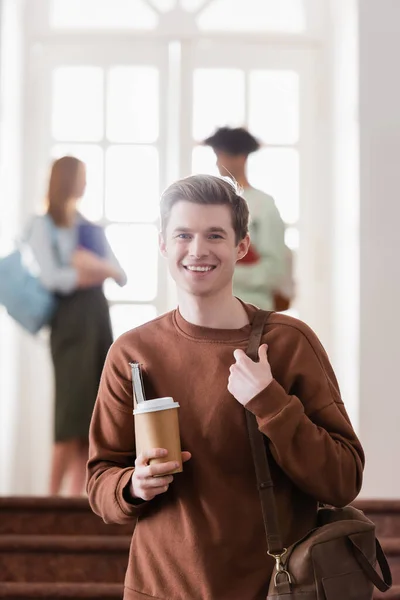 Étudiant joyeux tenant sac, carnet et tasse en papier — Photo de stock