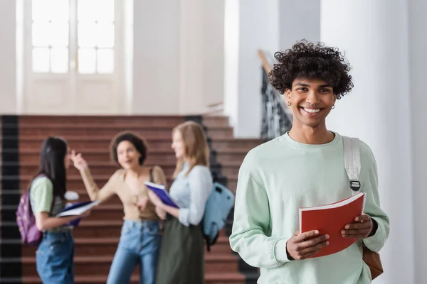 Afrikanischer Student mit Rucksack und Notizbuch blickt in Kamera — Stockfoto