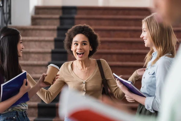 Cheerful african american student talking near interracial friends with notebooks — Stock Photo