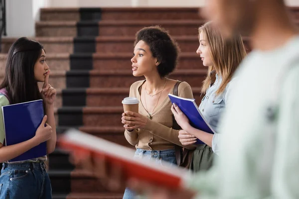 Asiatico studente mostrando segreto gesto vicino interrazziale amici con notebook e caffè — Foto stock