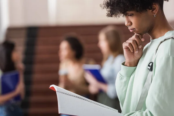 Vista lateral de un estudiante afroamericano mirando un cuaderno en la universidad - foto de stock
