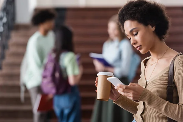African american student with coffee to go using smartphone — Stock Photo