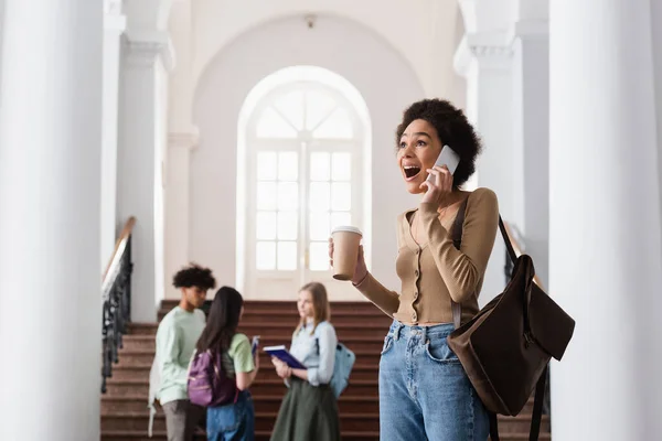 Excited african american student with coffee talking on cellphone — Stock Photo