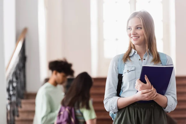 Fröhlicher Student mit Notizbuch schaut in der Uni weg — Stockfoto