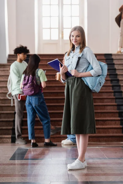 Étudiant souriant avec sac à dos et cahier regardant la caméra à l'université — Photo de stock