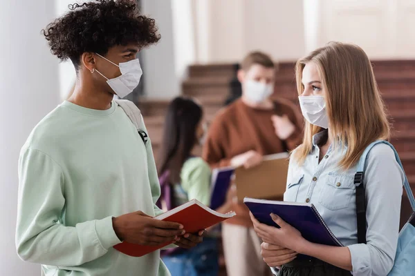 Multiethnische Studenten in medizinischen Masken mit Notizbüchern an der Universität — Stockfoto